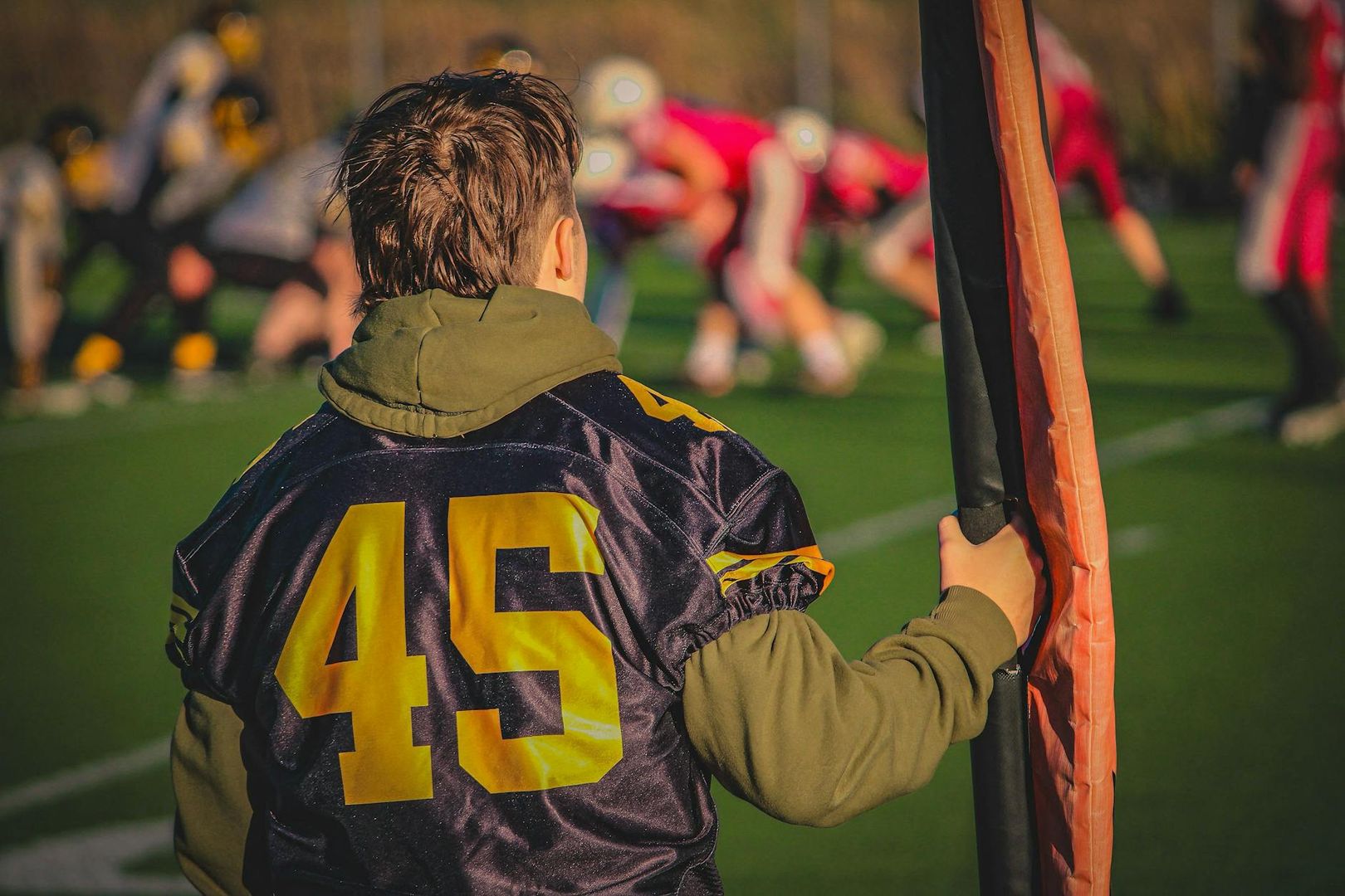Ungdom i tröja nr 45 vid en amerikansk fotbollsmatch, tittar på spelet.